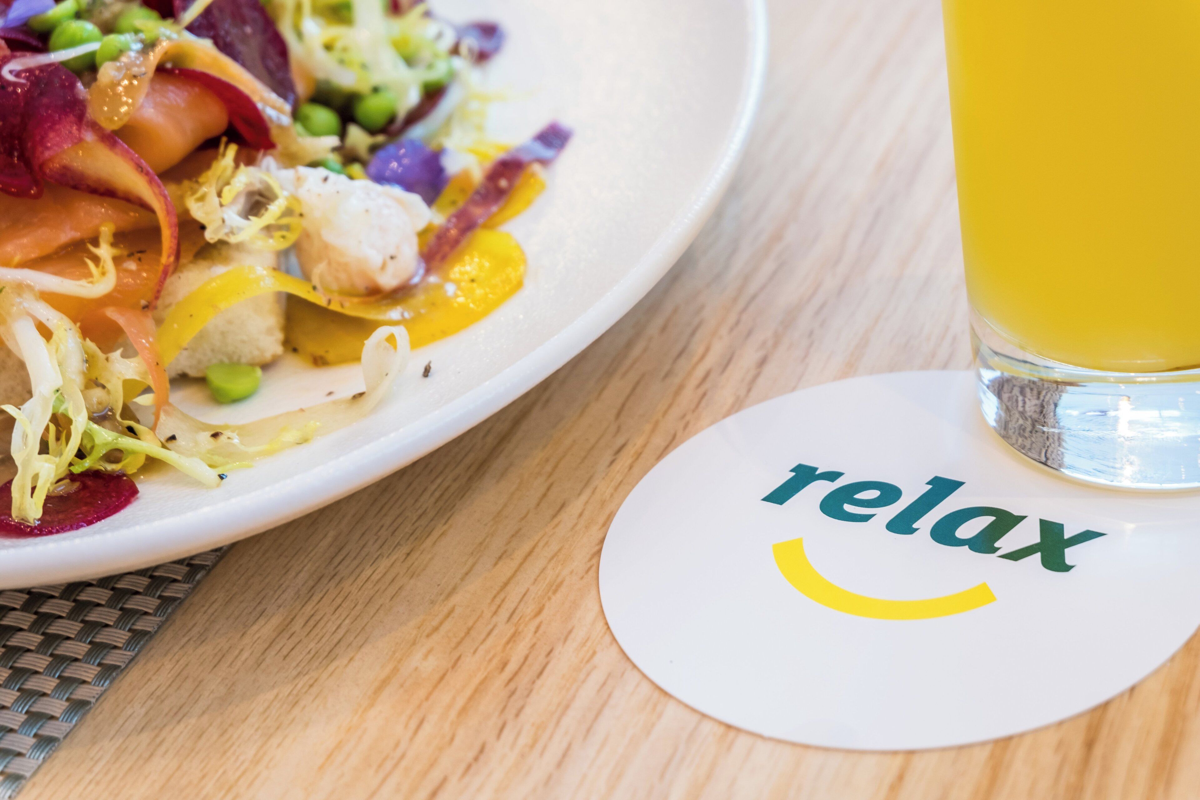 A plate of food with a glass of yellow beverage and a coaster with the word 'relax' on it.