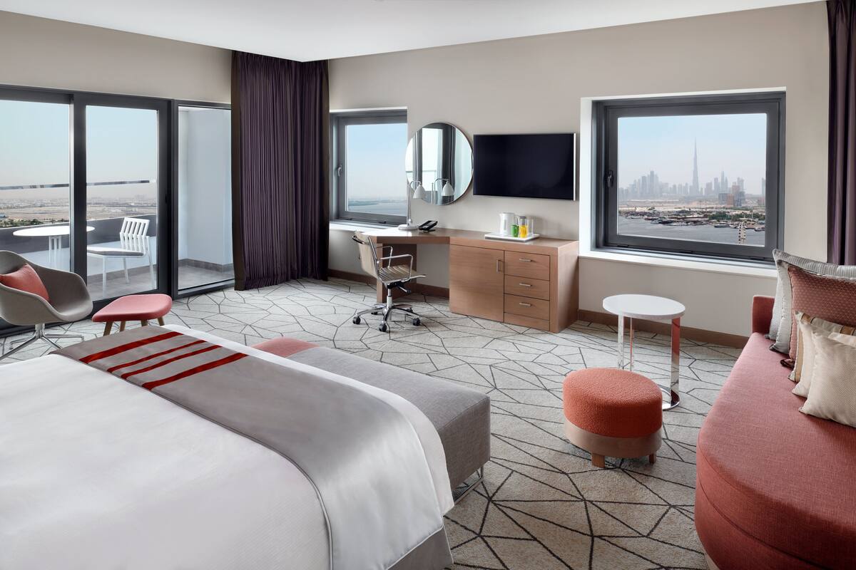 Une chambre d’hôtel avec un grand lit, un bureau avec une chaise, une télévision et une vue sur le panorama de la ville.