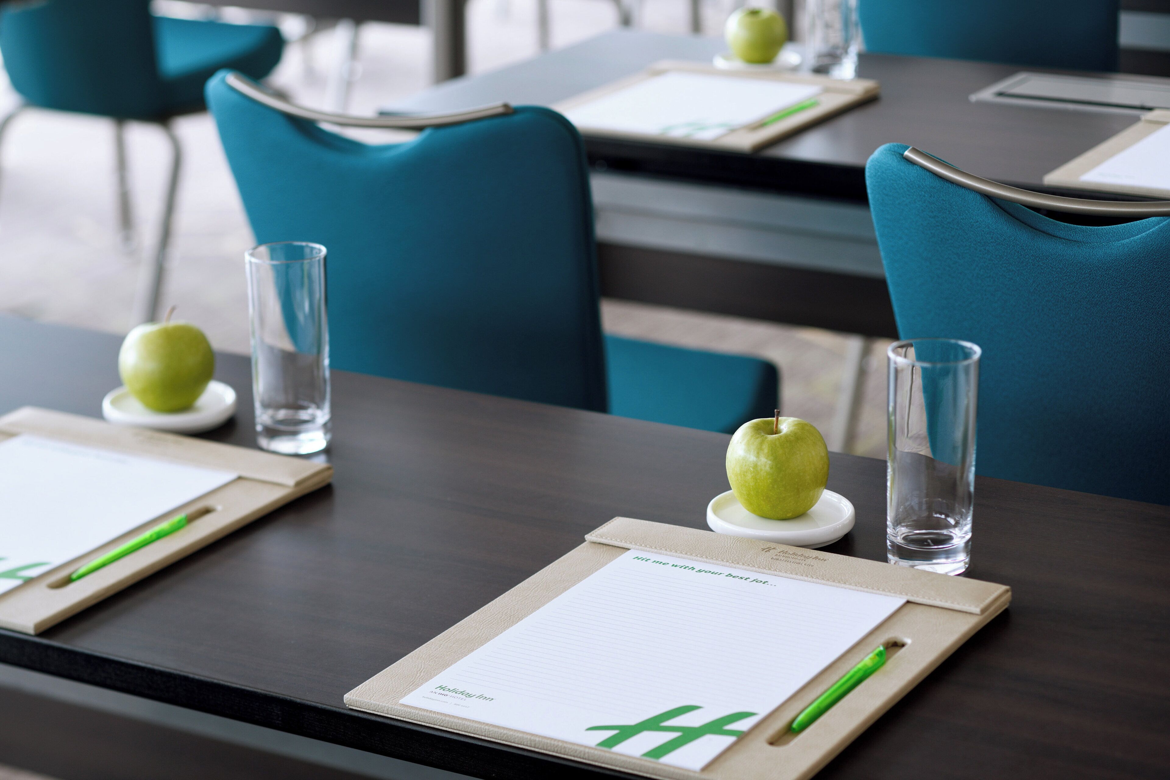 A hotel room with a neatly arranged table featuring a menu, a green apple, and a glass of water.