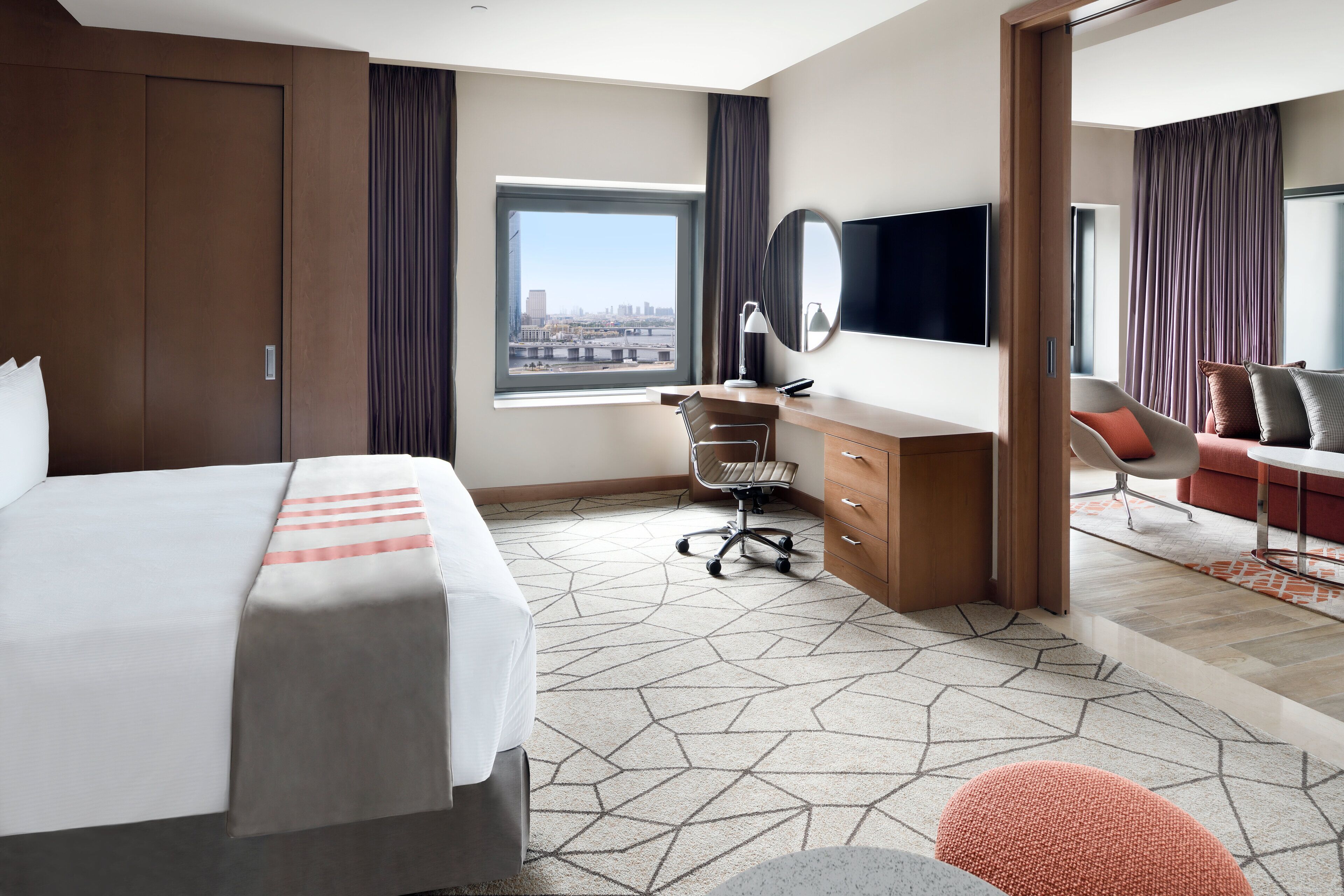 A hotel room with a bed, a desk, a chair, a TV, and a view of the city.