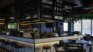 Een bar met krukken en tafels, een toonbank met flessen en borden die verschillende drankjes aangeven.