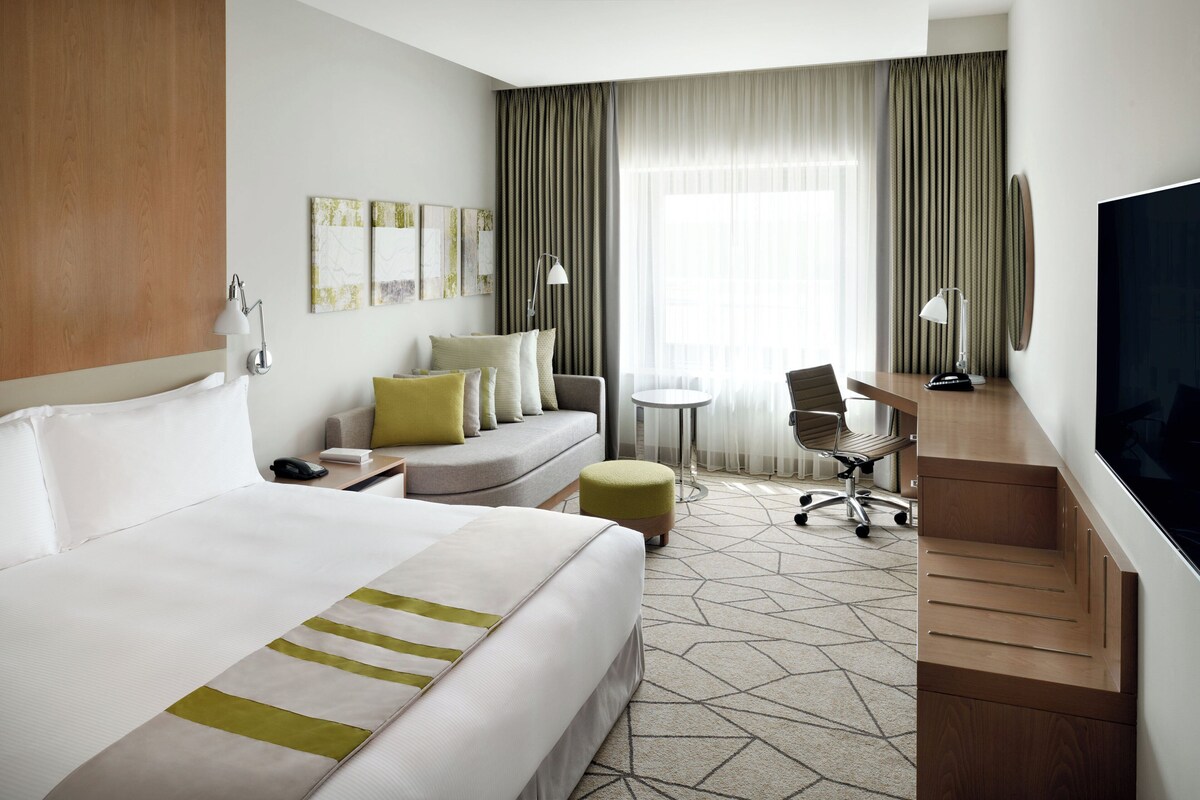 Une chambre d’hôtel avec un grand lit, un bureau, une chaise, une petite table et un téléviseur.