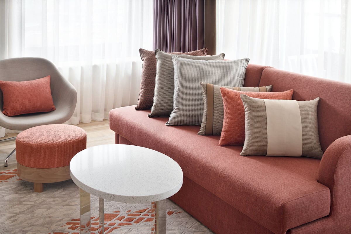 Un salon moderne avec un canapé rouge, de nombreux coussins, une table ronde blanche et un fauteuil.