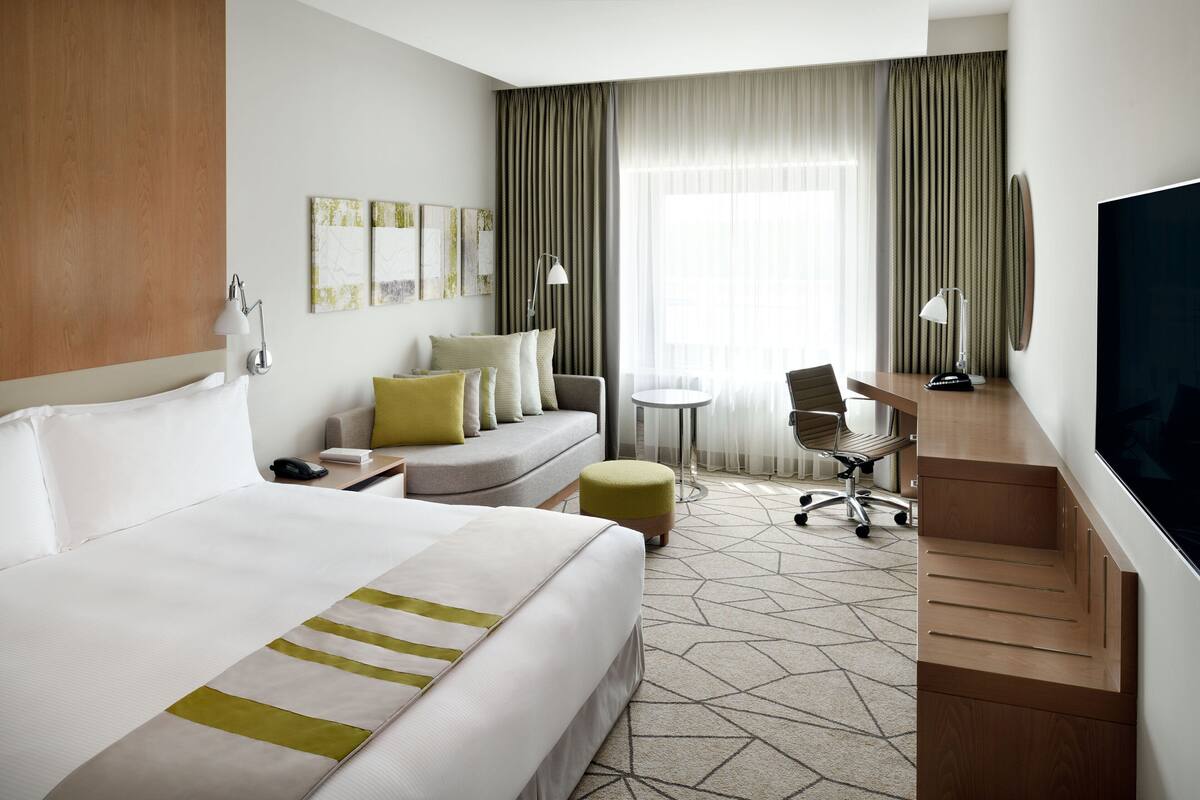 Une chambre d’hôtel avec un grand lit, un bureau, une chaise, une petite table et un téléviseur.