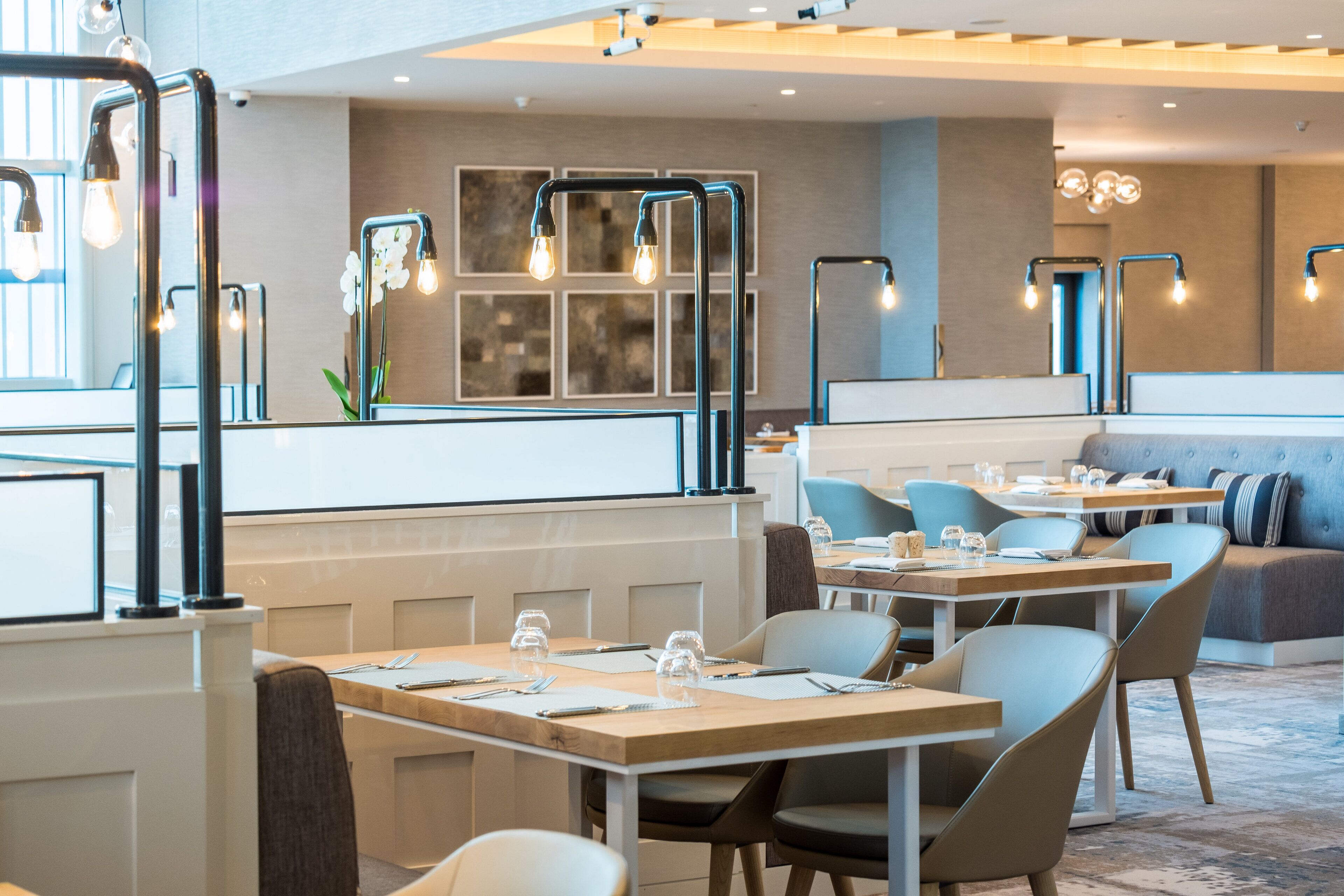 A modern restaurant with tables set for dining, a seating area with couches, and decorative light fixtures.