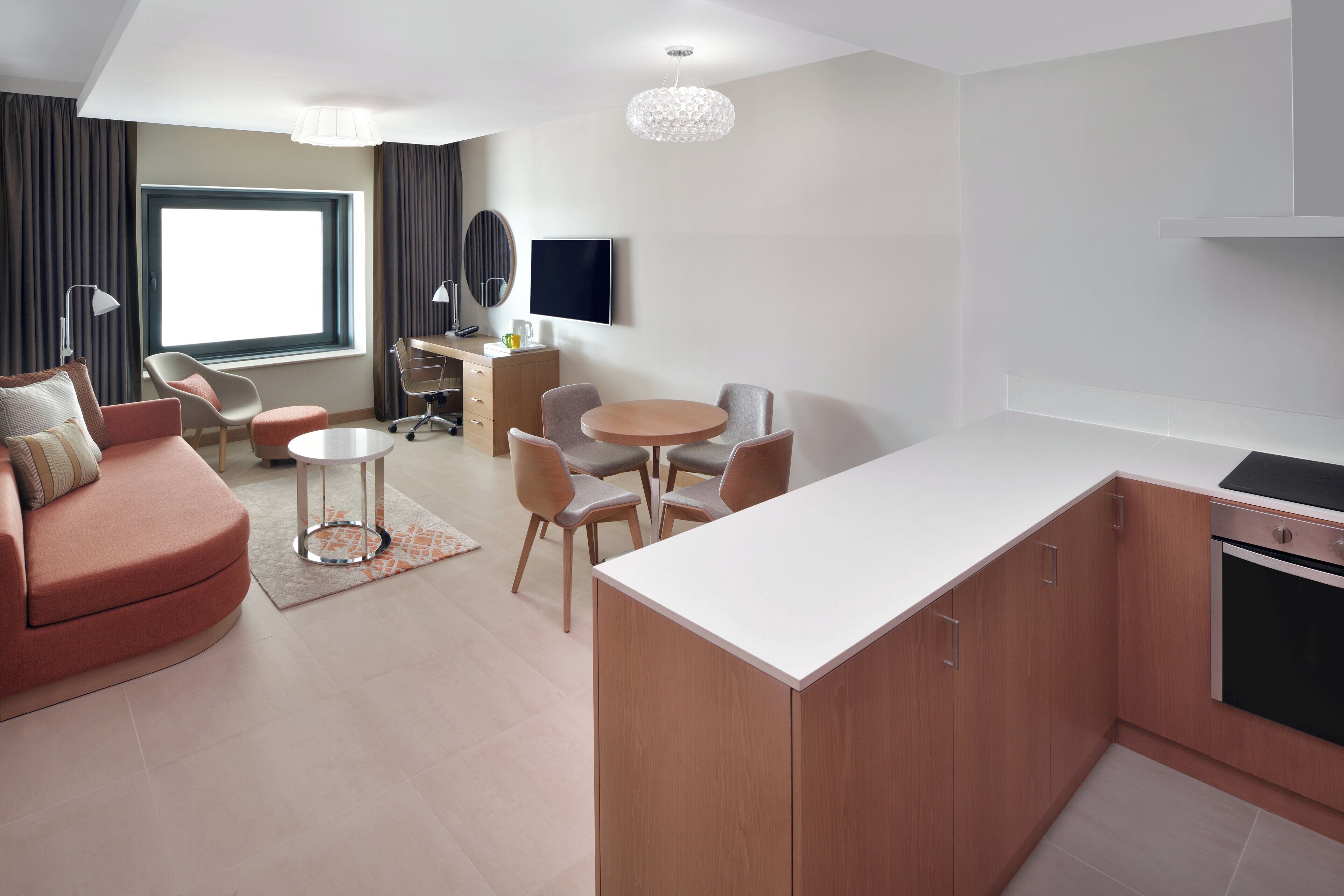 Ein modernes Wohnzimmer mit einer Couch, einem Esstisch und Stühlen, einer Küchenzeile mit Herd und einem großen Fenster, das für natürliches Licht sorgt.