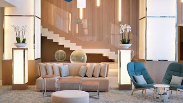 Un vestíbulo moderno con una escalera, un sofá, un taburete redondo y un sillón azul.