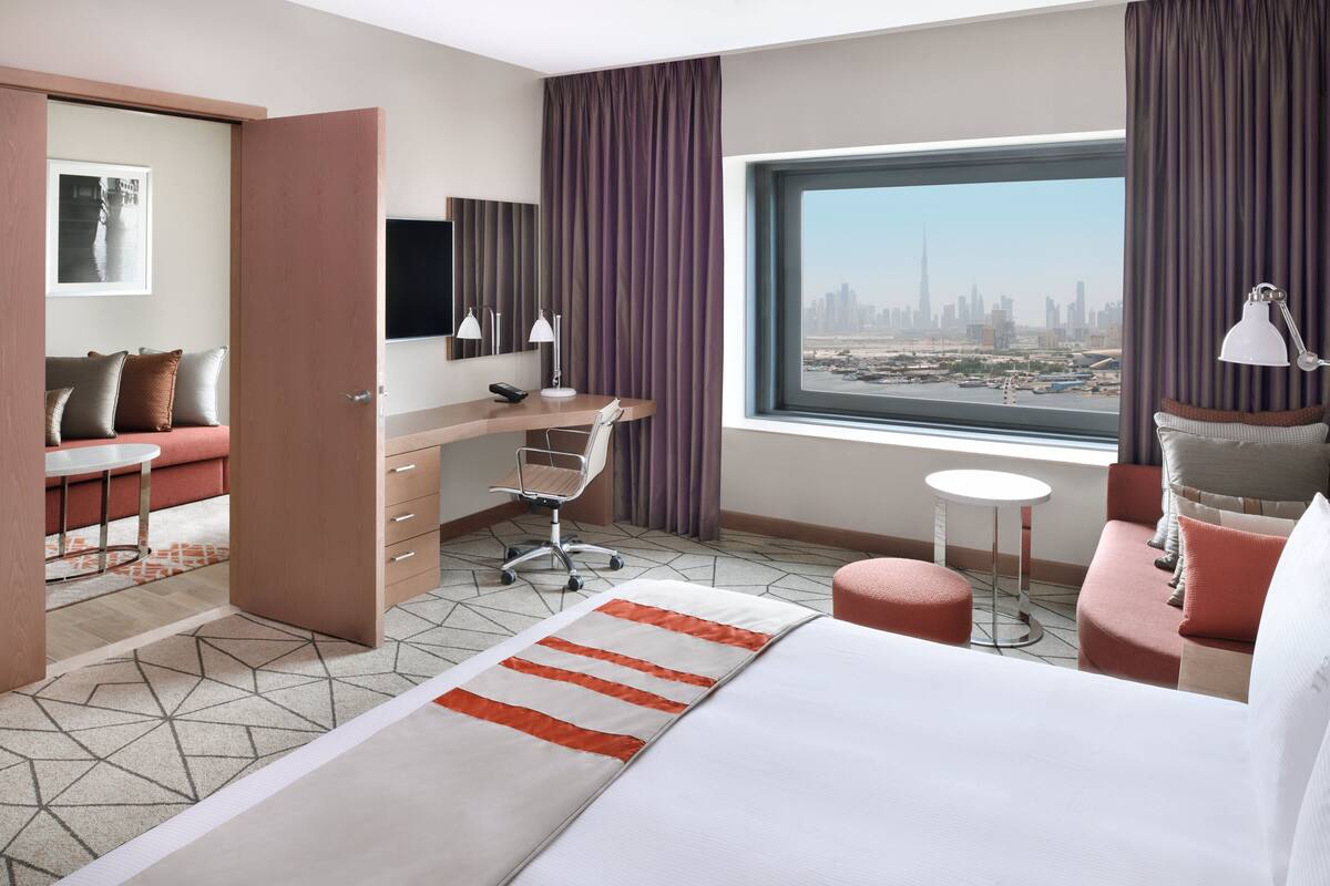 Une chambre d’hôtel moderne équipée d’un lit, d’un bureau, d’une chaise et d’une grande fenêtre donnant sur la ville.