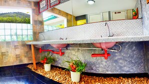 A bathroom with a large sink, two plants, and a window with a view of greenery. - The Pelican Larry Hostel (Cali)
