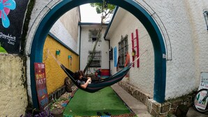 A hammock in an outdoor area with a white wall, a yellow wall, and a blue archway. - The Pelican Larry Hostel (Cali)