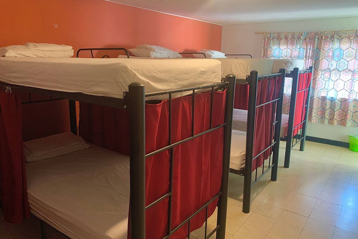 A dormitory room with bunk beds, a window with patterned curtains, and a tiled floor.