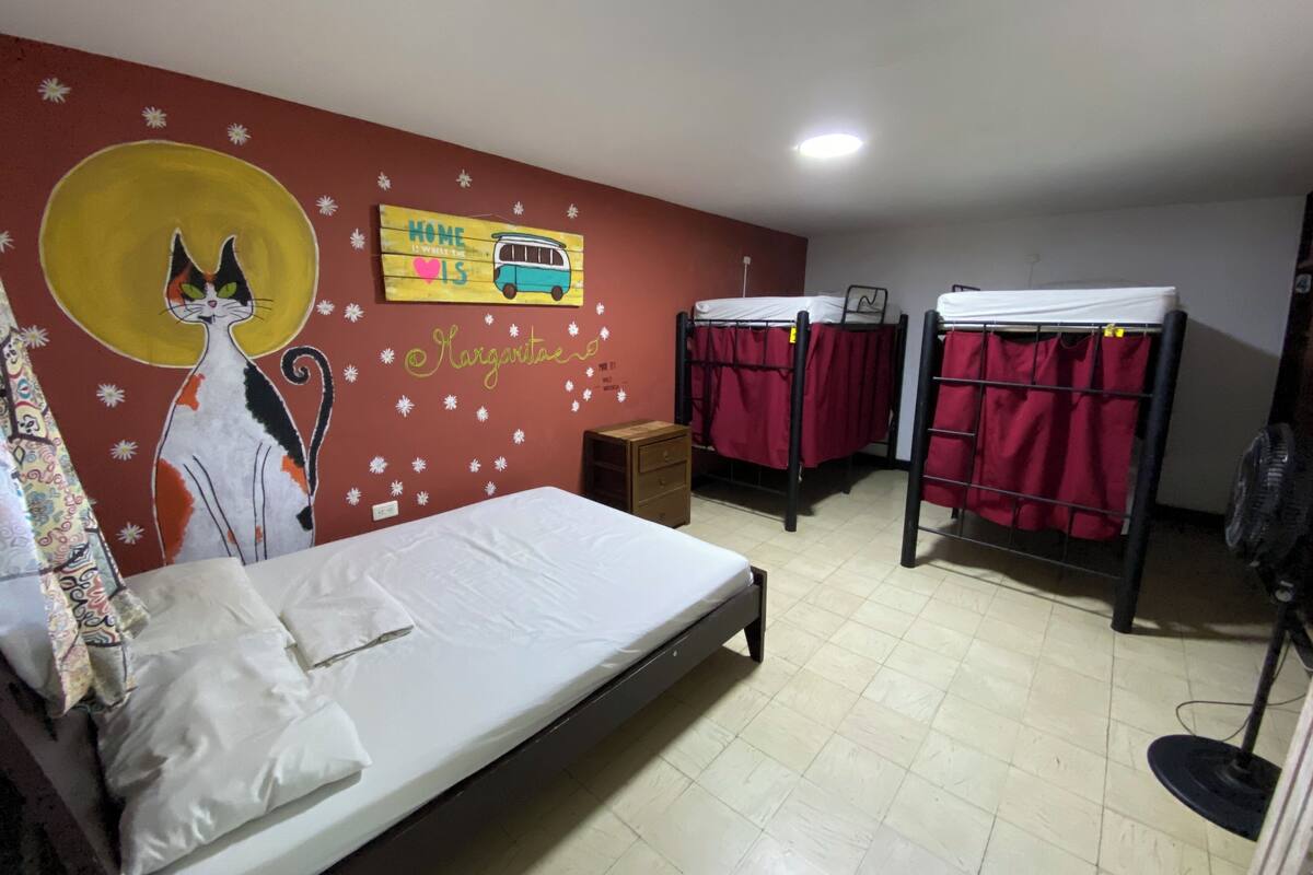 A dormitory room with a single bed, two bunk beds, a wall mural, and a small wooden cabinet.