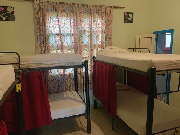 A dormitory room with bunk beds, patterned curtains, and a door with a window. - The Pelican Larry Hostel (Cali)