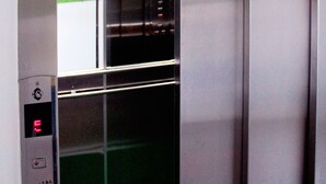 Een liftinterieur met metalen wanden en een groen tapijt.