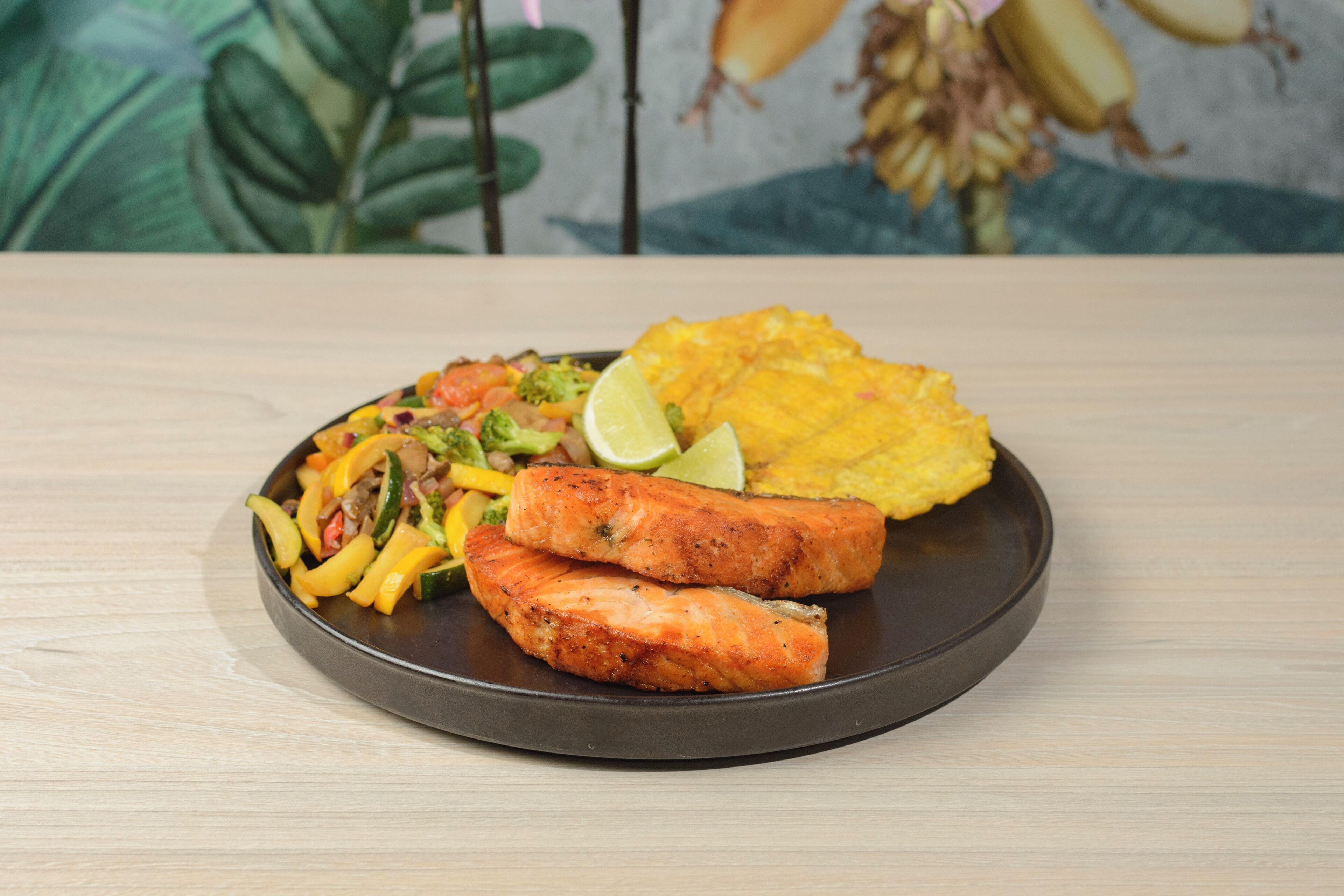 A plate of food with salmon, vegetables, and plantains on a dark plate.