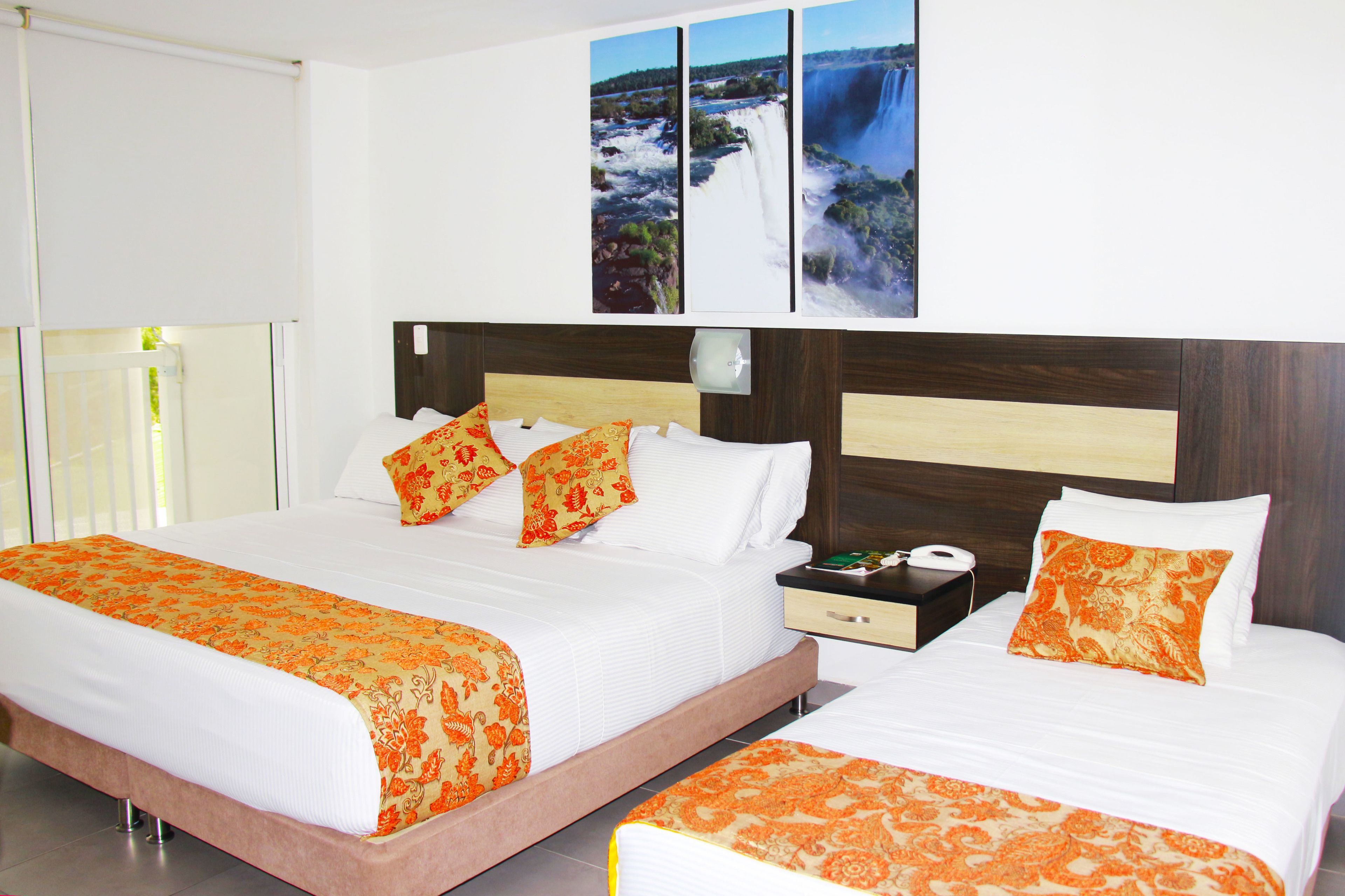 A hotel room with two beds, a nightstand, a phone, and a wall-mounted artwork of a waterfall.