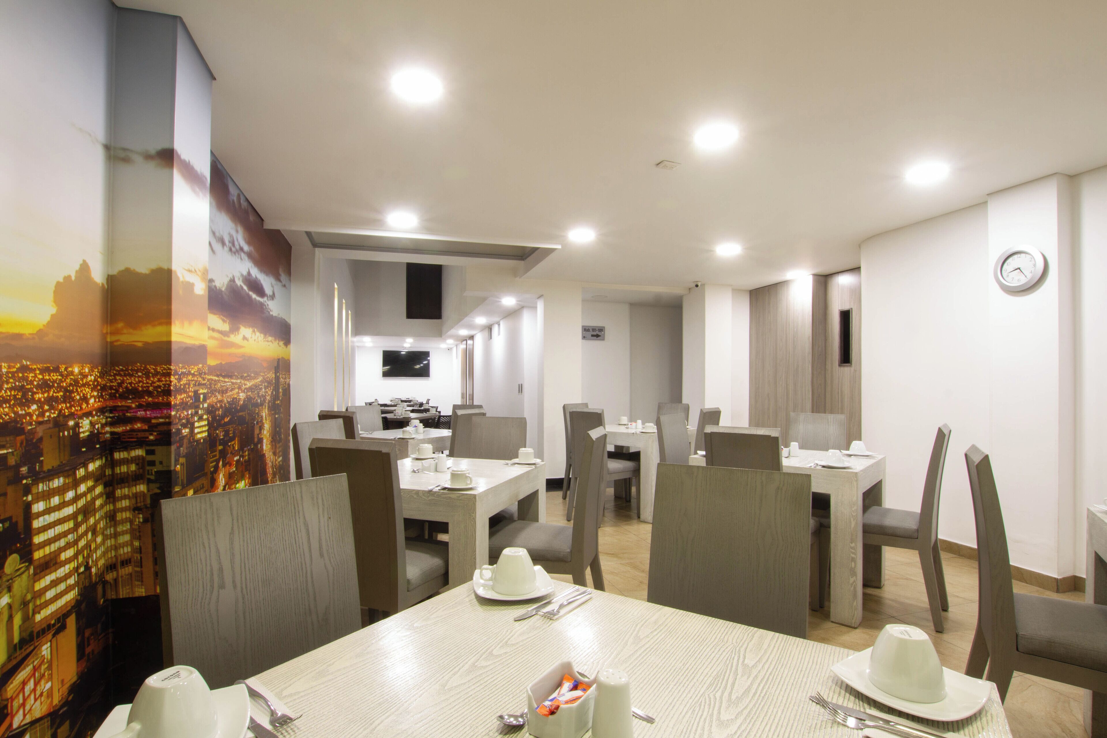 A hotel dining area with multiple tables and chairs, a view of a cityscape, and a clock on the wall.