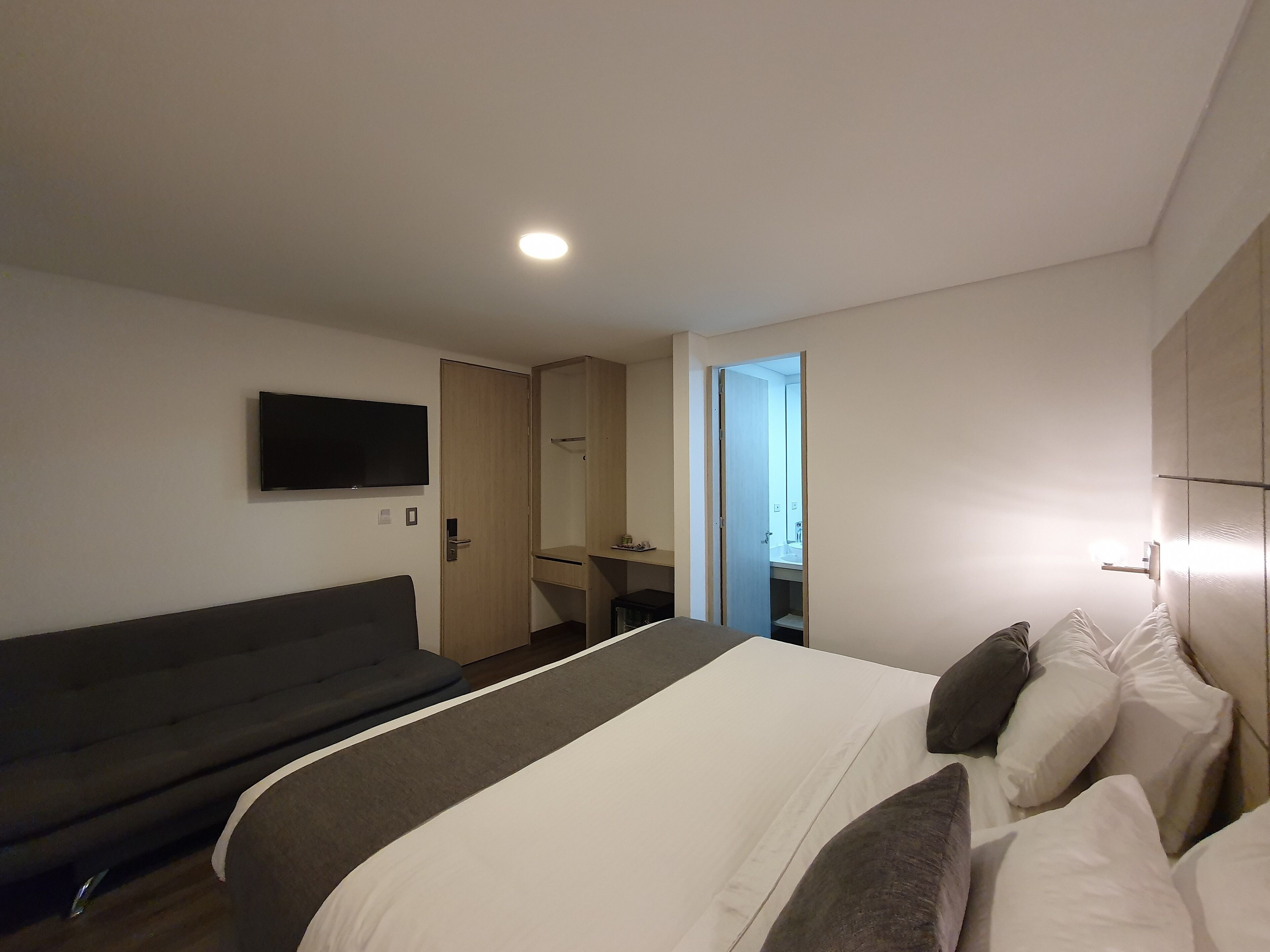 Een moderne hotelkamer met een bed, een bank, een televisie en een badkamer die door een open deur zichtbaar is.