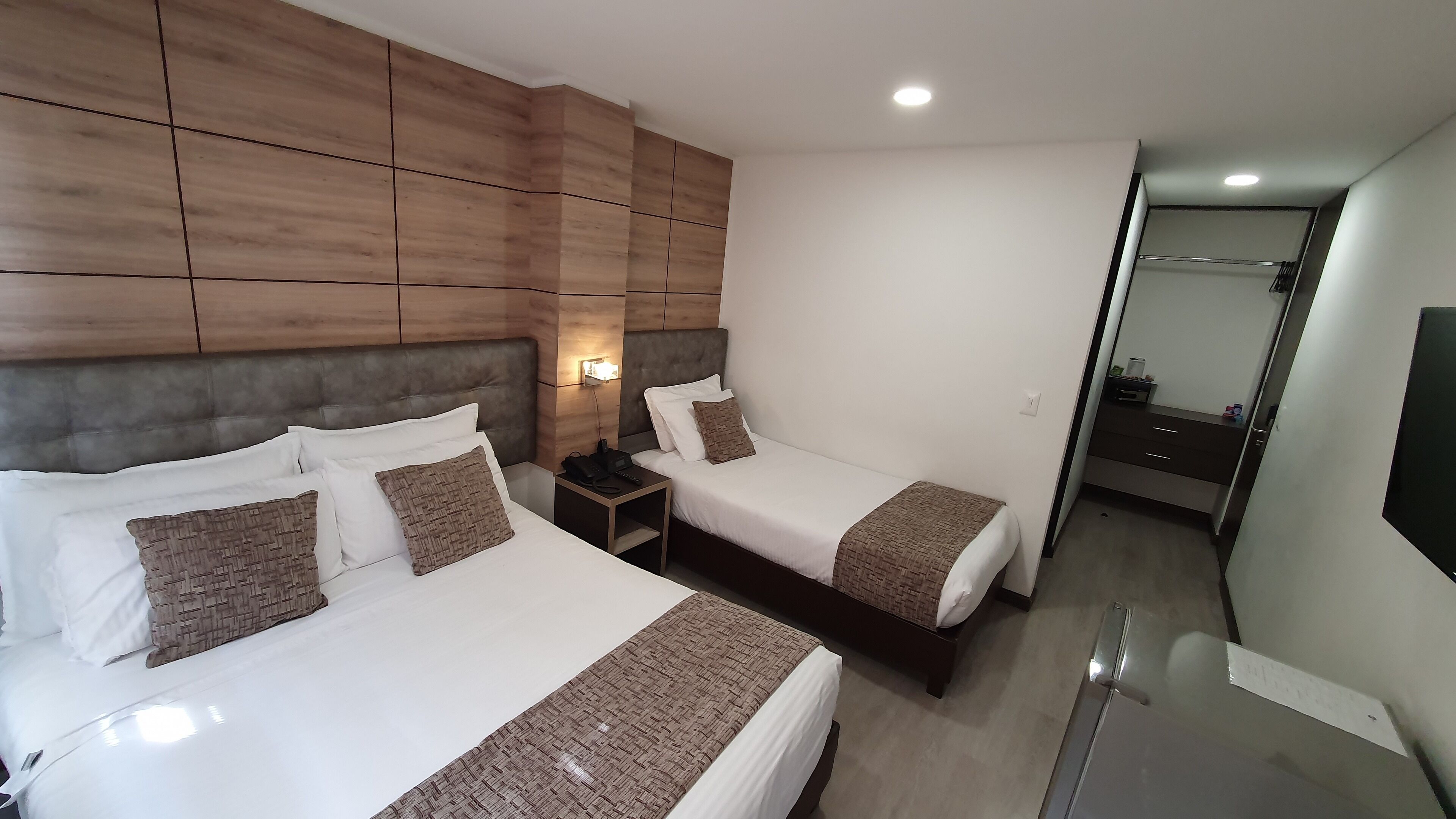 A hotel room with two beds, wooden paneling on the walls, a nightstand with a phone, and a mirror.