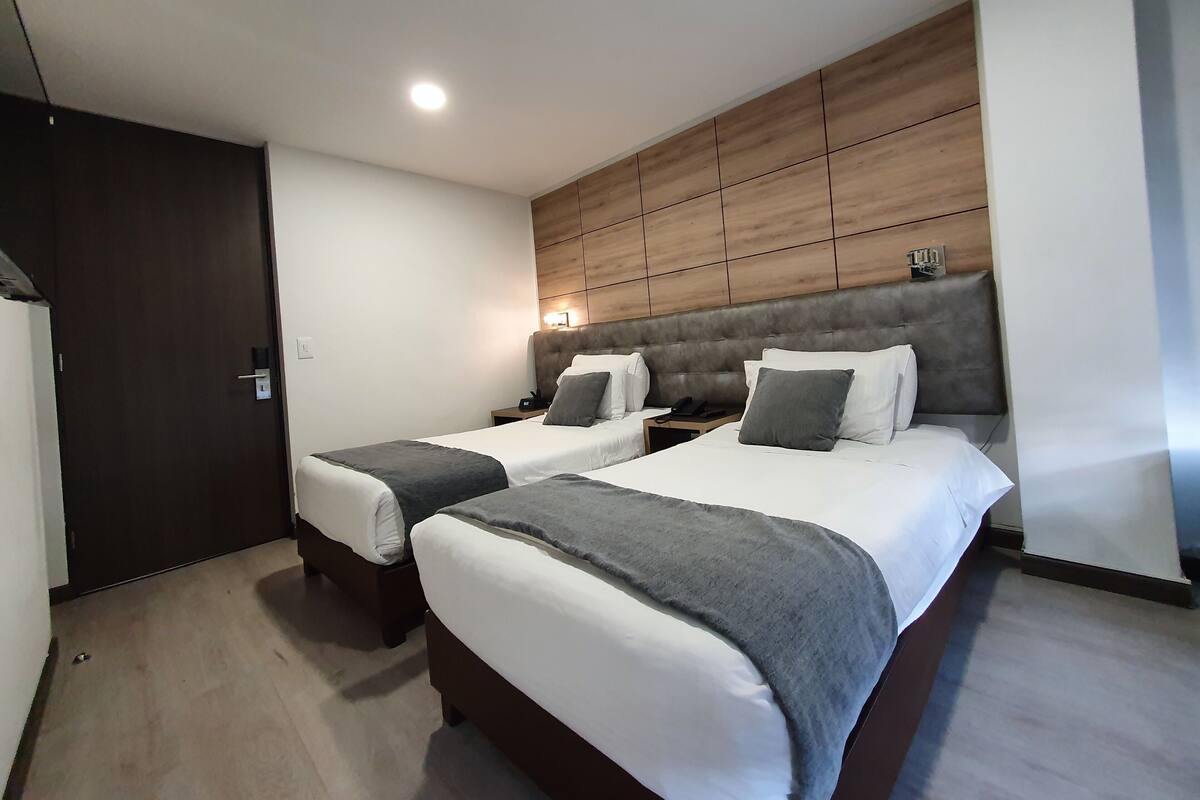 A hotel room with two beds, a wooden headboard, a nightstand with a phone, and a door.