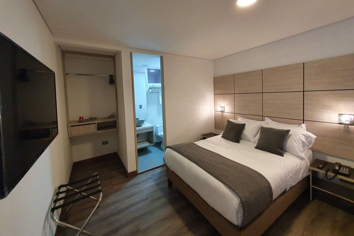 A modern hotel room with a large bed, bedside tables, a TV, and a walk-in closet.