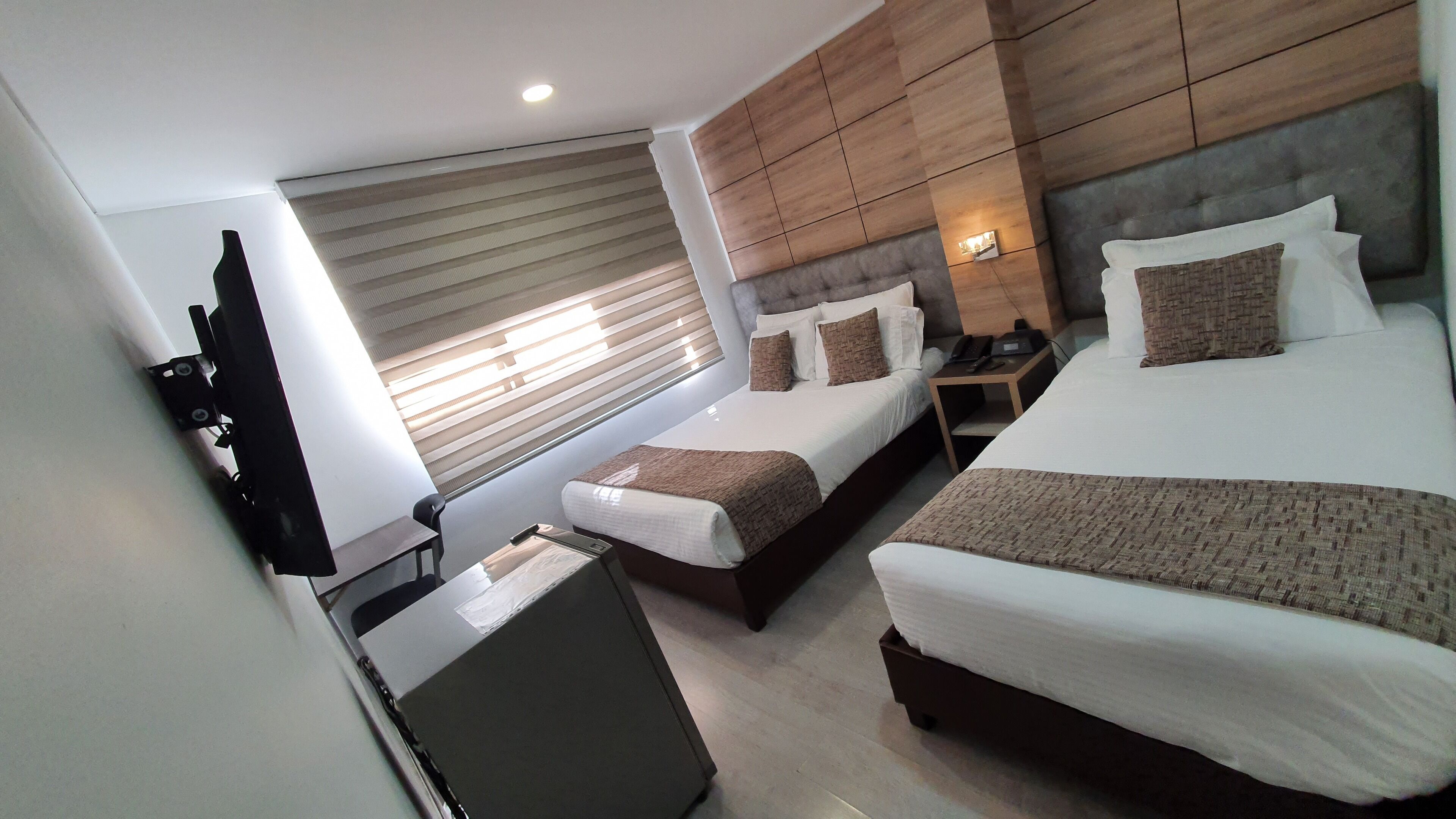 A hotel room with two beds, a desk, a chair, a wardrobe, and a window with blinds.
