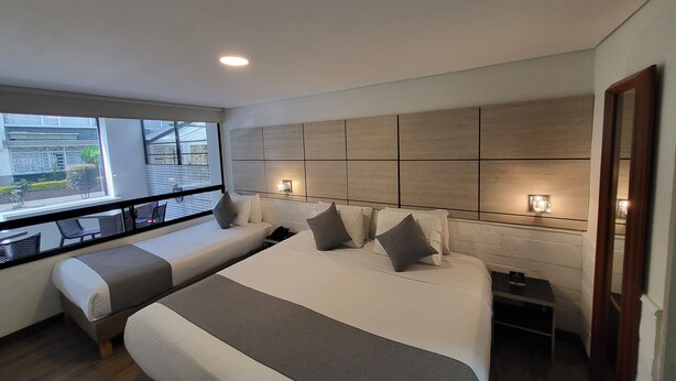 A modern hotel room with a large bed, a smaller sofa, a bedside table, and a view of the outside. - Bog Urban Hotel (Bogotá)