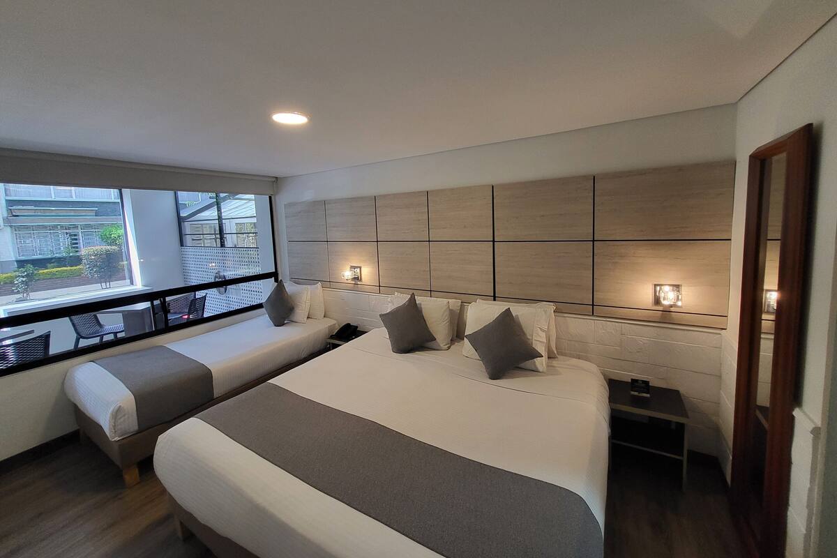 A modern hotel room with a large bed, a smaller sofa, a bedside table, and a view of the outside.