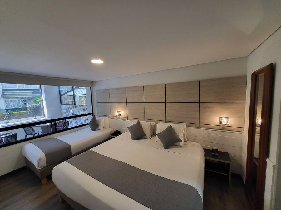 A modern hotel room with a large bed, a smaller sofa, a bedside table, and a view of the outside.