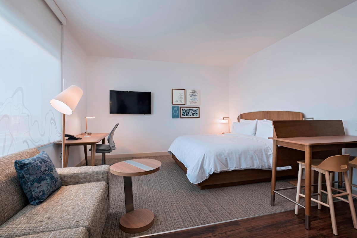 Una habitación de hotel moderna con cama, sofá, escritorio y televisor.