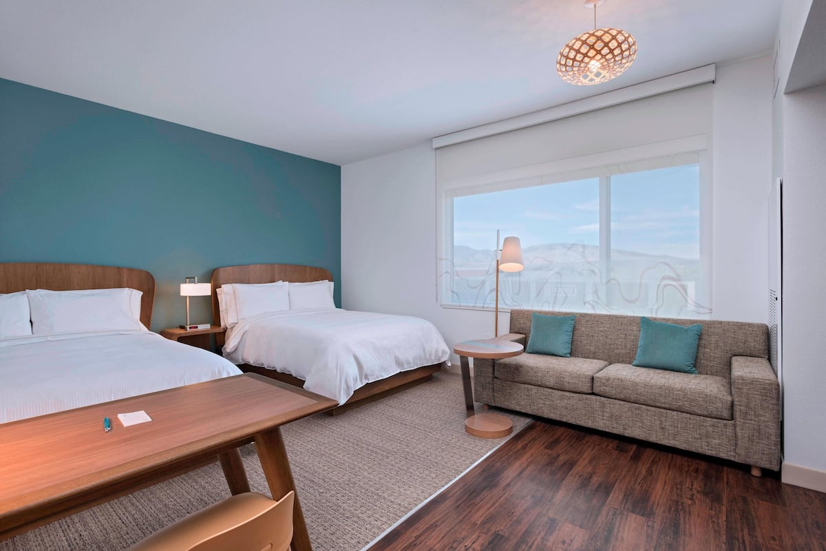 Una habitación de hotel moderna con dos camas, un sofá, una mesita y un ventanal con vistas.