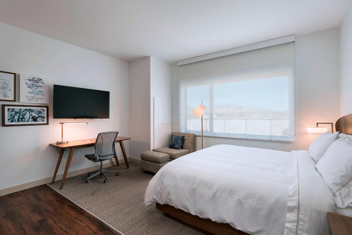 Habitación de hotel con cama, escritorio, silla y televisión en la pared.