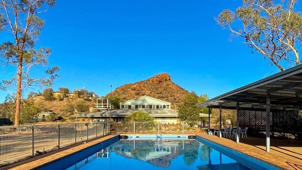 A swimming pool with a clear view of a mountain in the background, surrounded by trees and a fenced area. - Arkaroola Wilderness Sanctuary (Arkaroola Village)