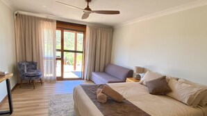 A bedroom with a bed, a chair, a sofa, a ceiling fan, and a view through a glass door. - Arkaroola Wilderness Sanctuary (Arkaroola Village)