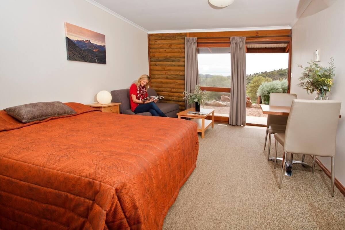 A hotel room with a large bed, a desk, a chair, a small table, and a window with curtains.