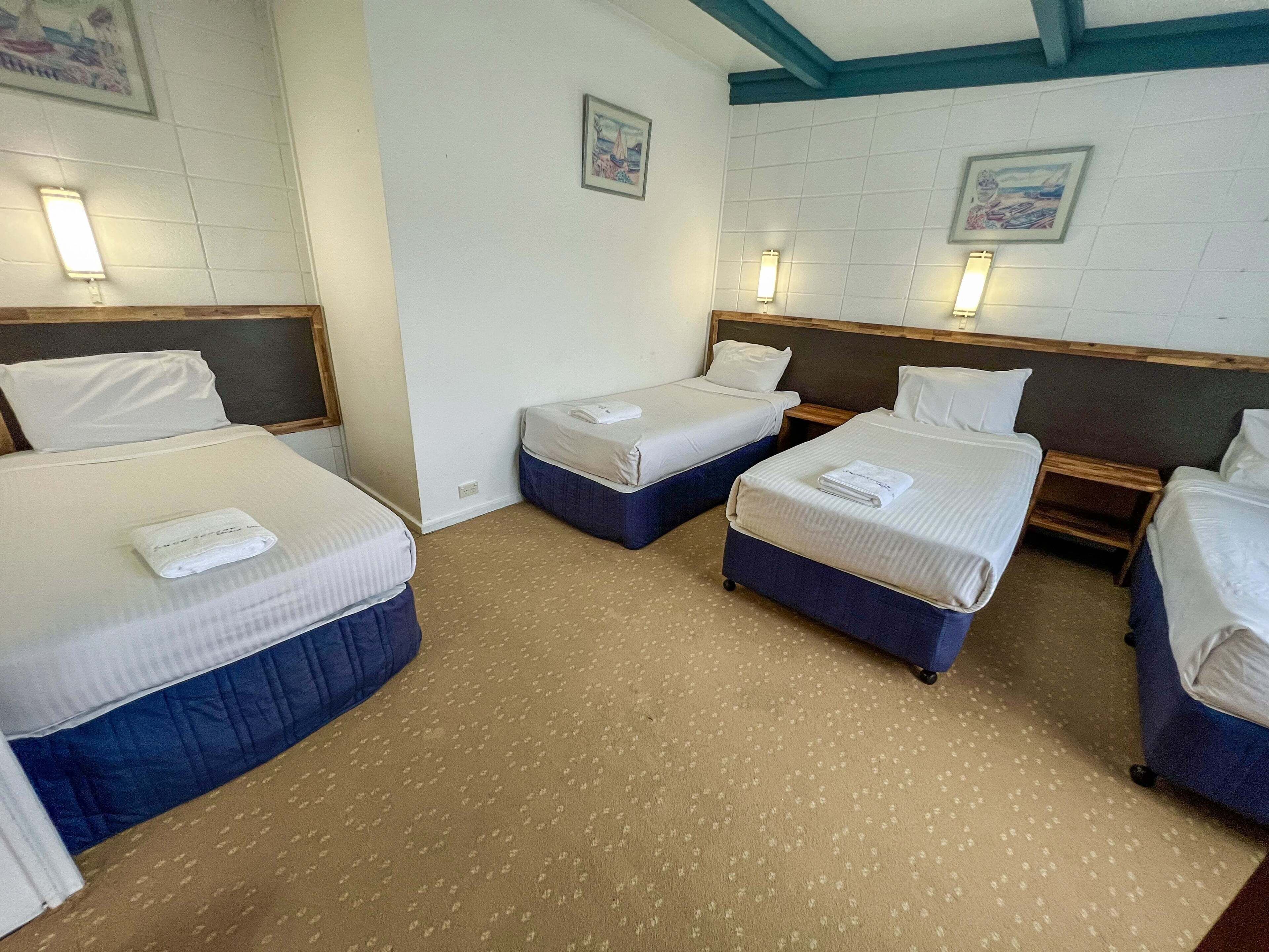 A hotel room with four beds arranged in a square layout, each with a pillow and a folded towel.