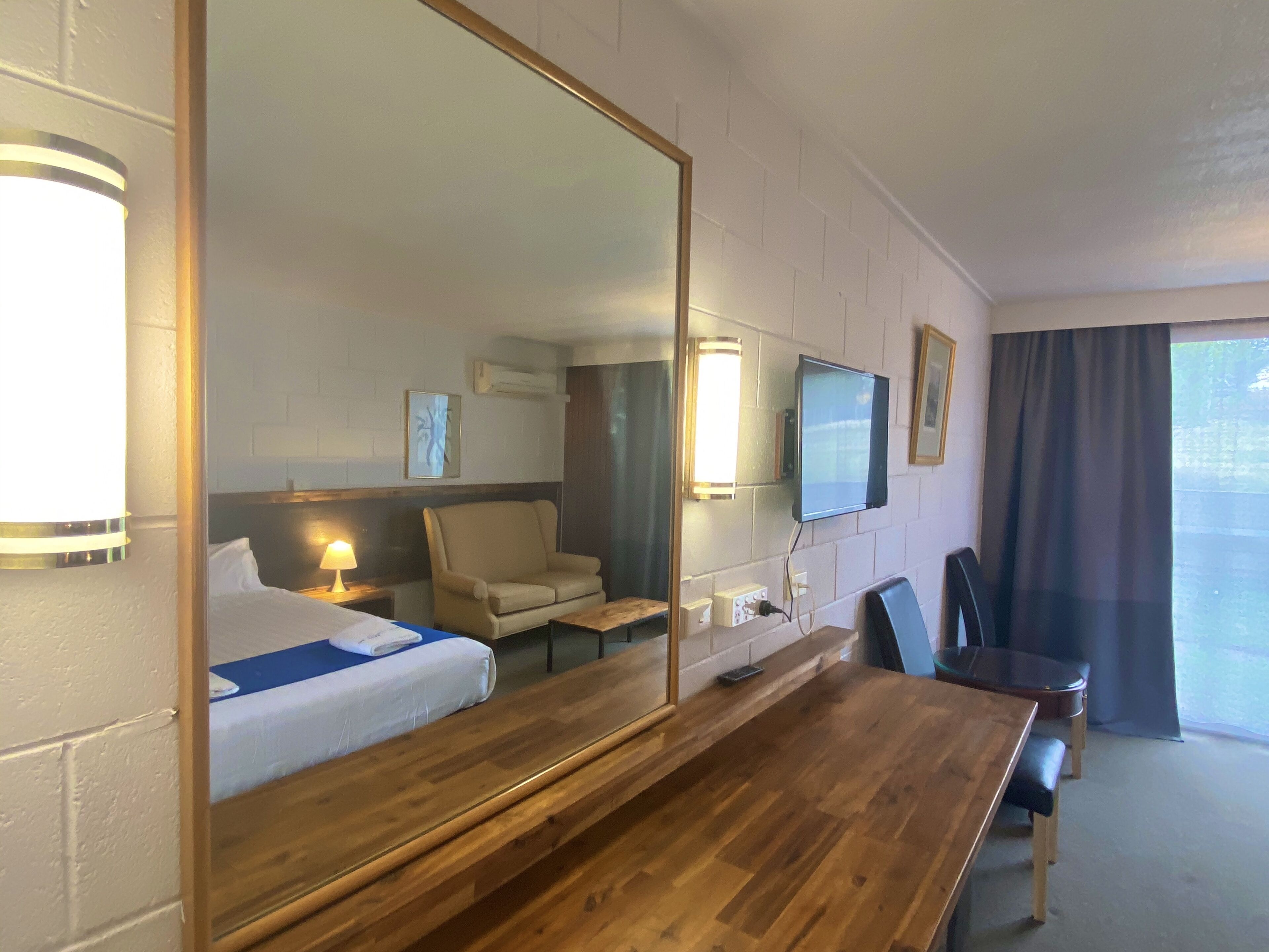 A hotel room with a large bed, a wooden table, a sofa, a TV, and a large mirror.