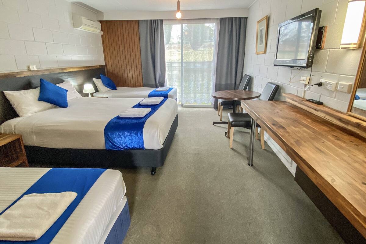 A hotel room with two beds, a wooden desk, a television, and a view of the outdoors.