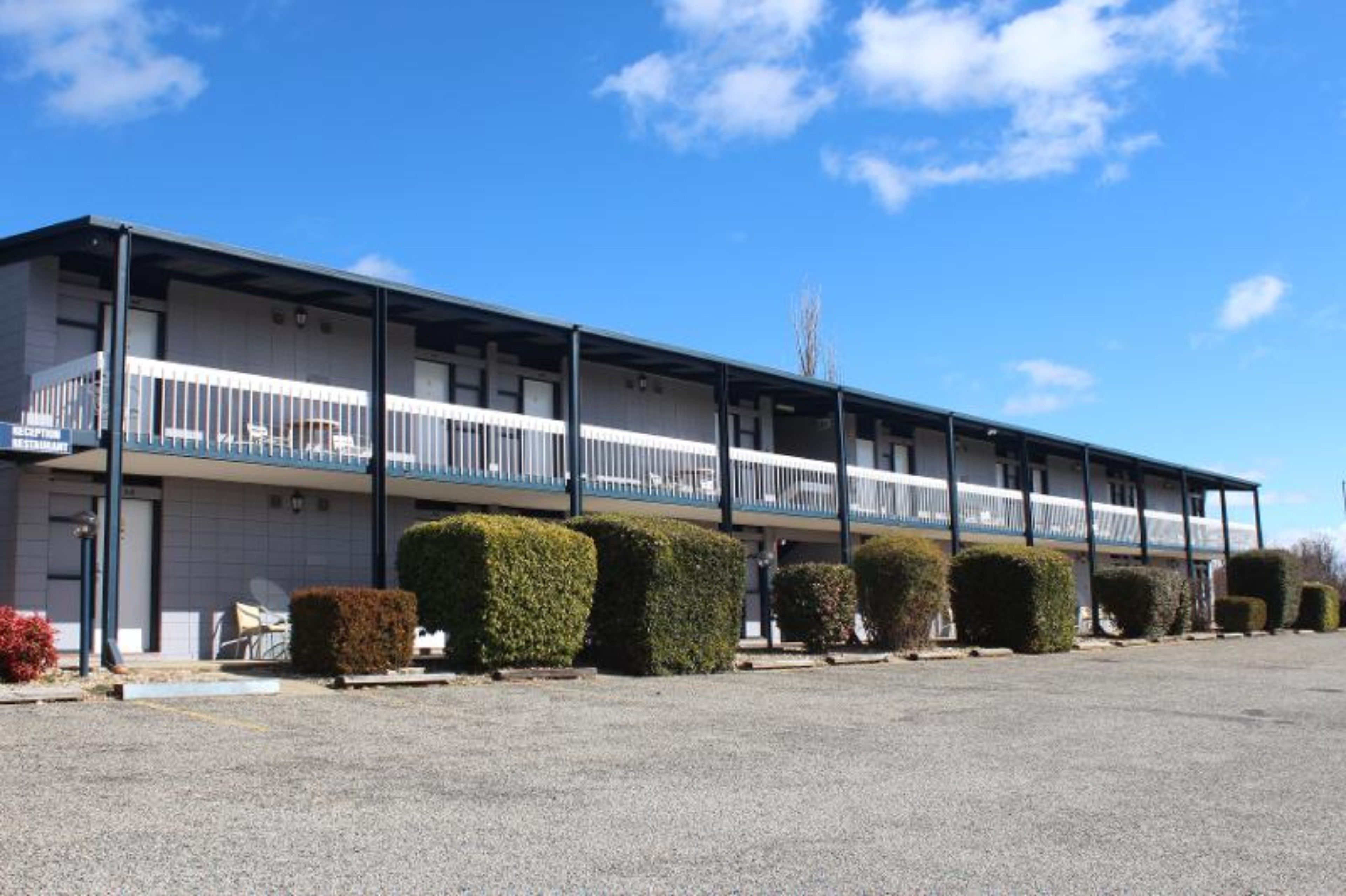 Un motel composé d’un bâtiment à deux étages, d’un espace de stationnement couvert et d’arbustes soigneusement taillés.