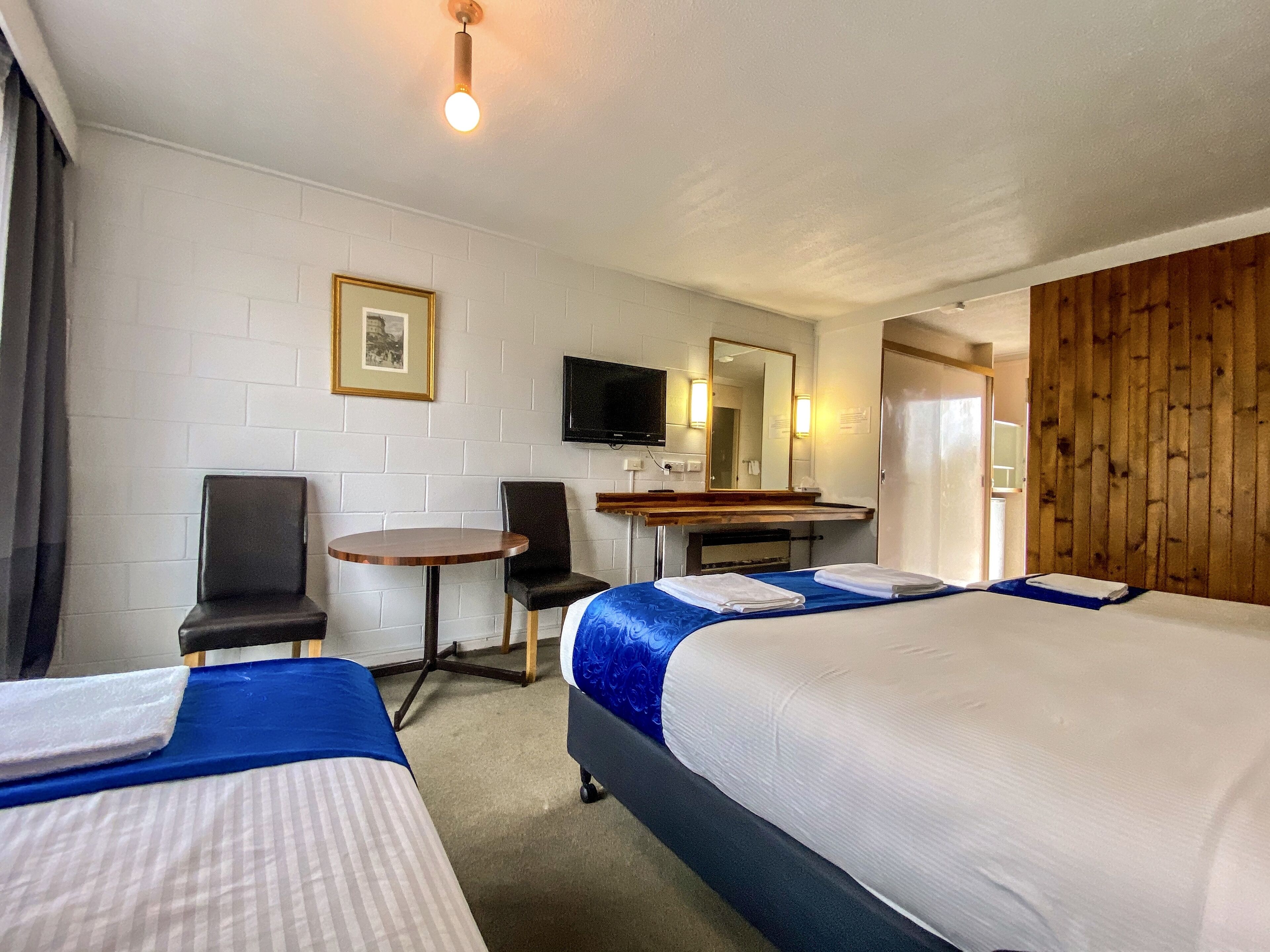 Una habitación de hotel con dos camas, un escritorio, una silla, un televisor y una pared de madera.