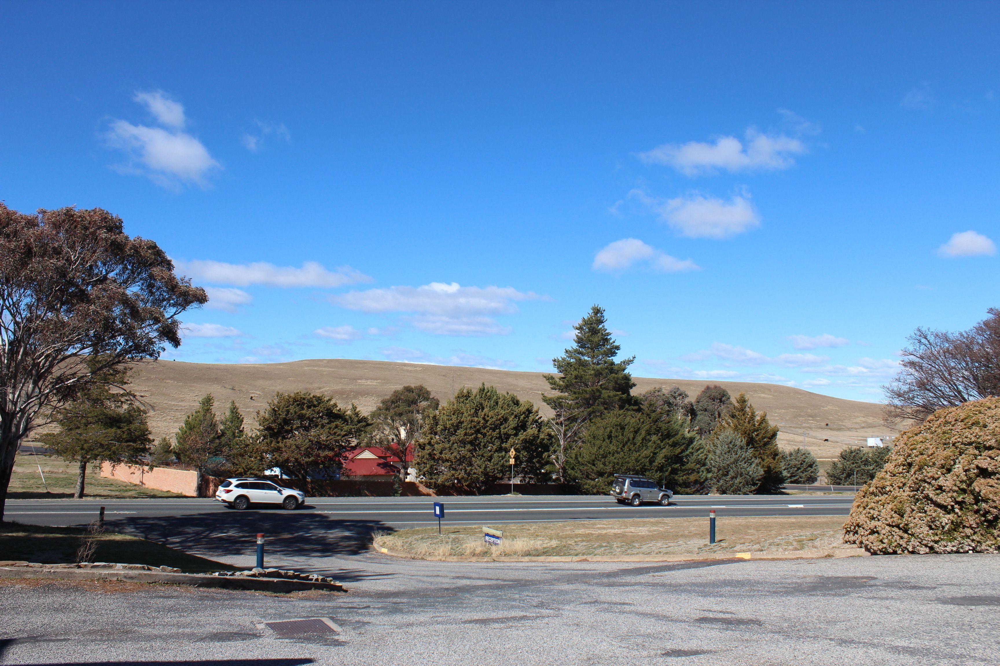 A parking lot with a red building in the background, surrounded by trees and hills.