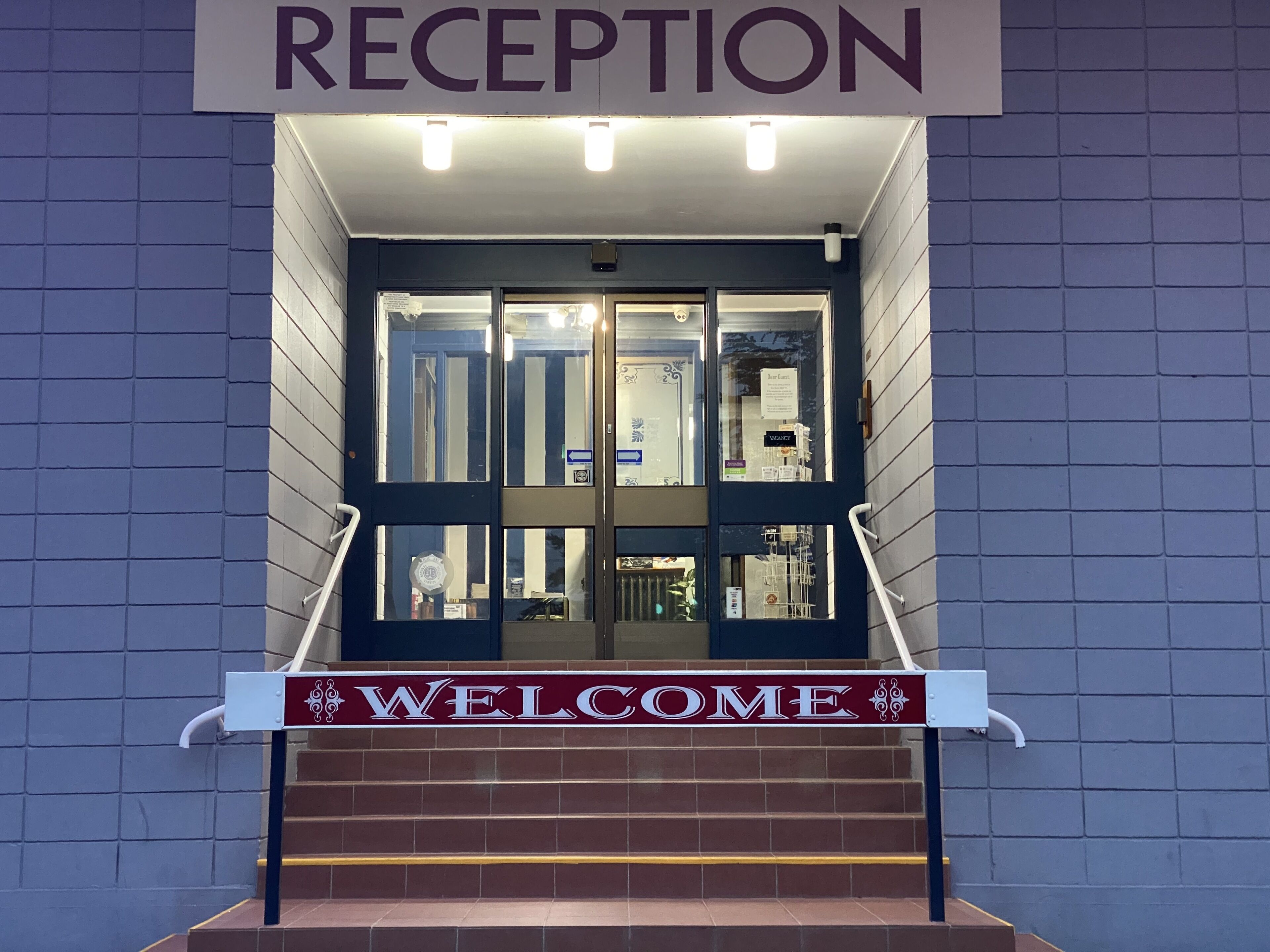 Una zona de recepción con un letrero que dice 'RECEPTION' sobre la entrada y un letrero de 'WELCOME' en las escaleras.