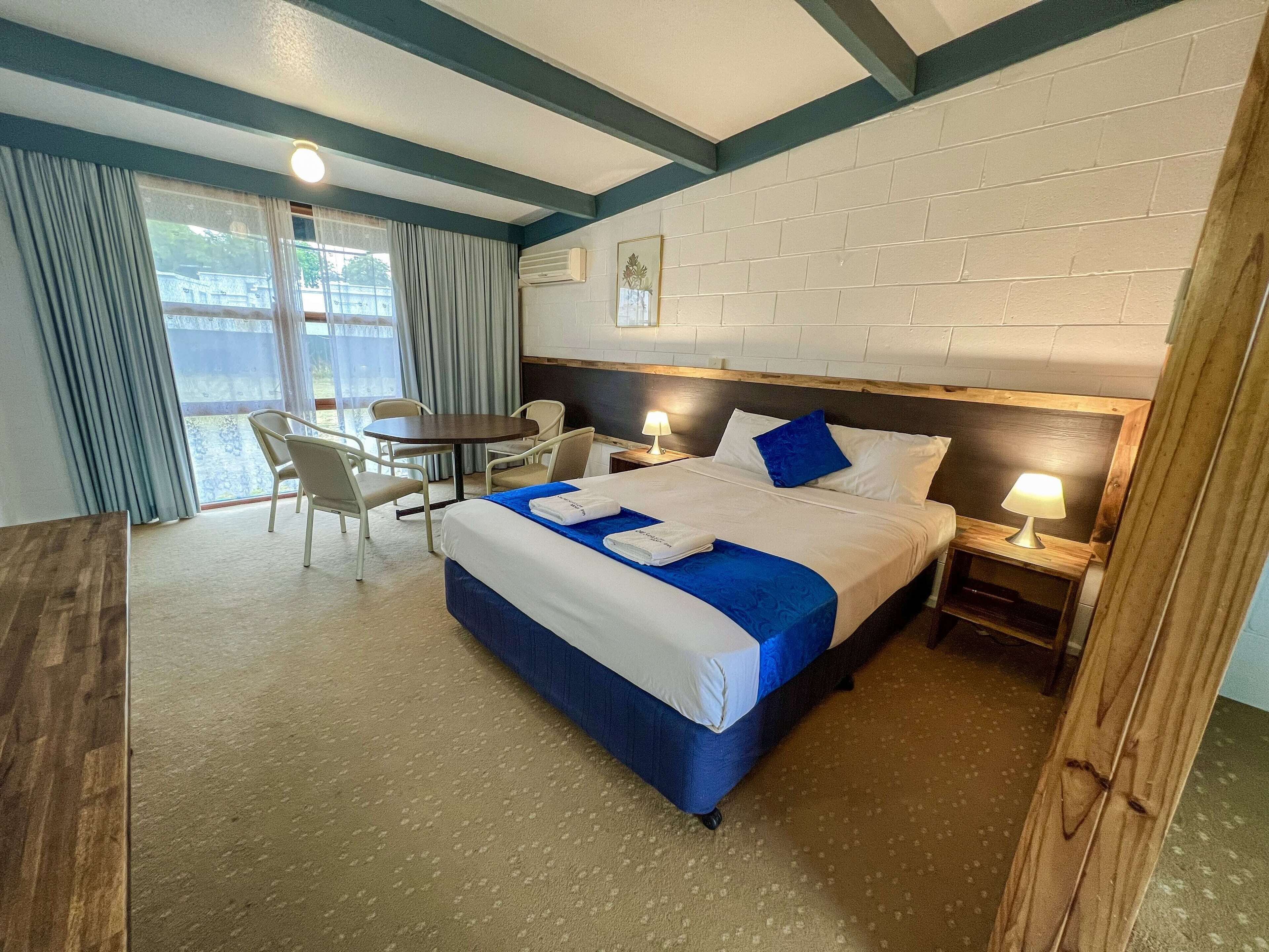 A hotel room with a bed, a desk, and a chair. There is a window with curtains and an air conditioning unit on the wall.