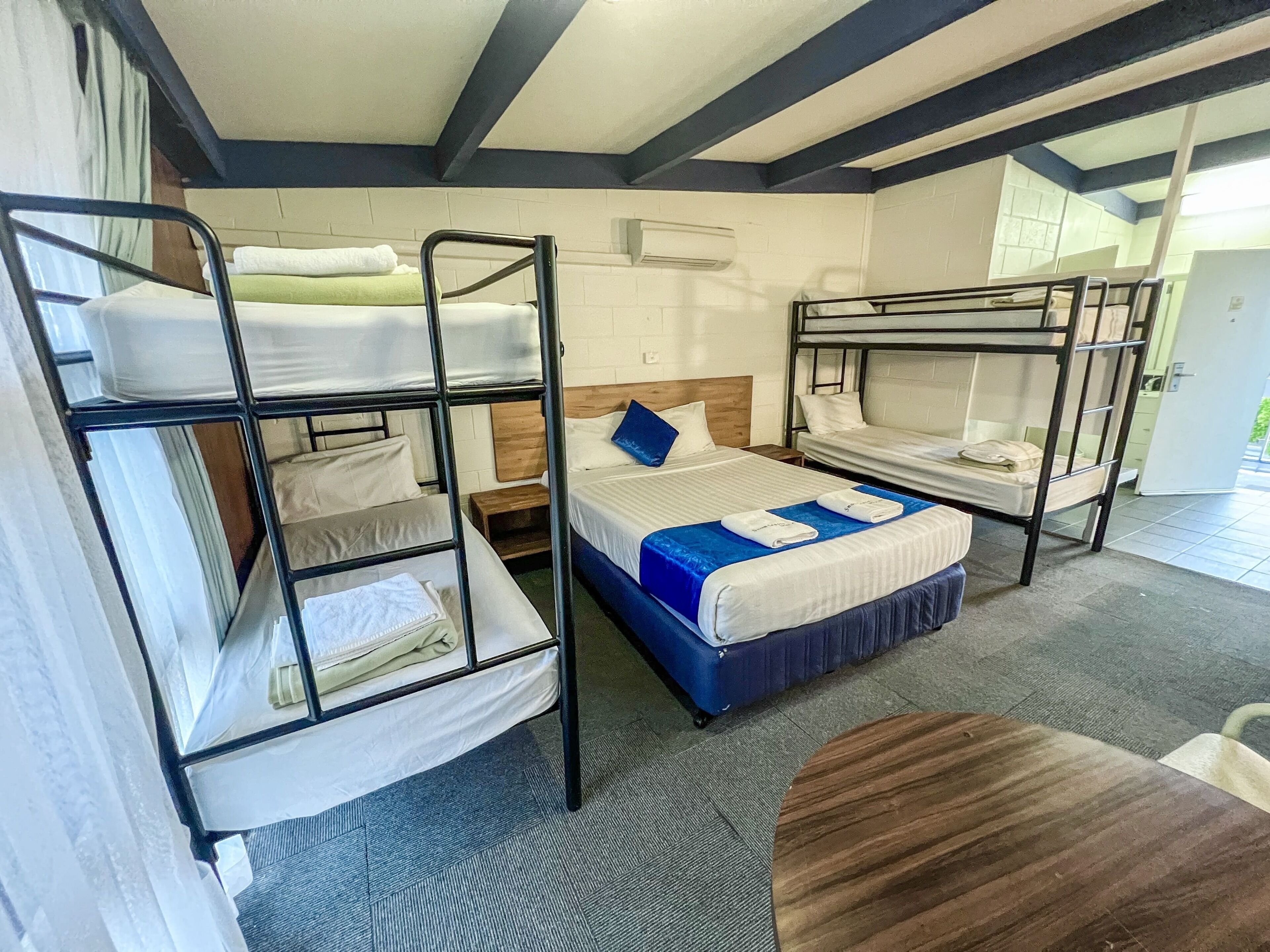 Une chambre de dortoir avec des lits superposés, une tête de lit en bois, une couvre-lit bleue et une petite table en bois.