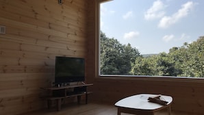 A wooden room with a large window, a television on a stand, and a small table with chopsticks. - Dabut (Seogwipo)