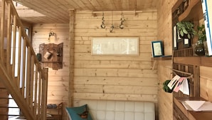 A wooden cabin interior with a white cushioned bench, wooden walls, and a staircase. - Dabut (Seogwipo)