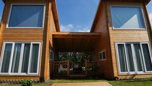 A modern wooden cabin with two large windows on each side, a covered porch, and a small garden area. - Dabut (Seogwipo)