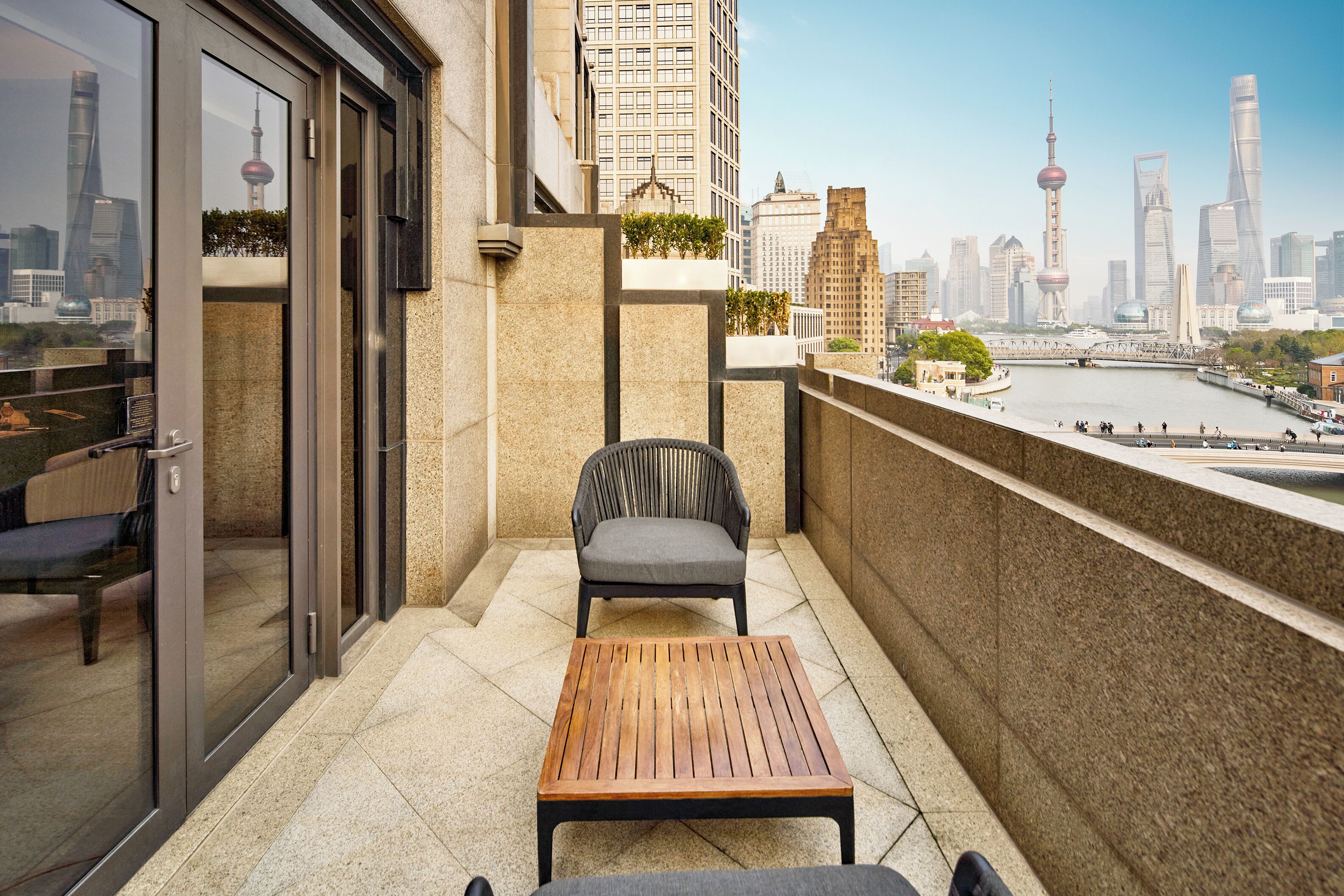 Ein Balkon mit Tisch und Stuhl, eine Glastür und Blick auf eine Stadtlandschaft mit einem Turm.
