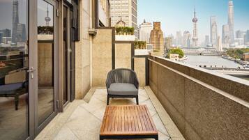 Ein Balkon mit Tisch und Stuhl, eine Glastür und Blick auf eine Stadtlandschaft mit einem Turm.