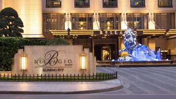 Entrada de un hotel con un letrero que dice "BELLA GIO" y una fuente decorativa.